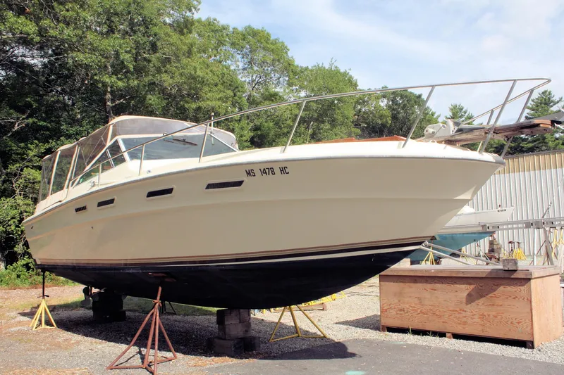 The Image of 1980 Sea Ray 300 Weekender boat on stands, outdoors, with trees and a building in the background. - 0