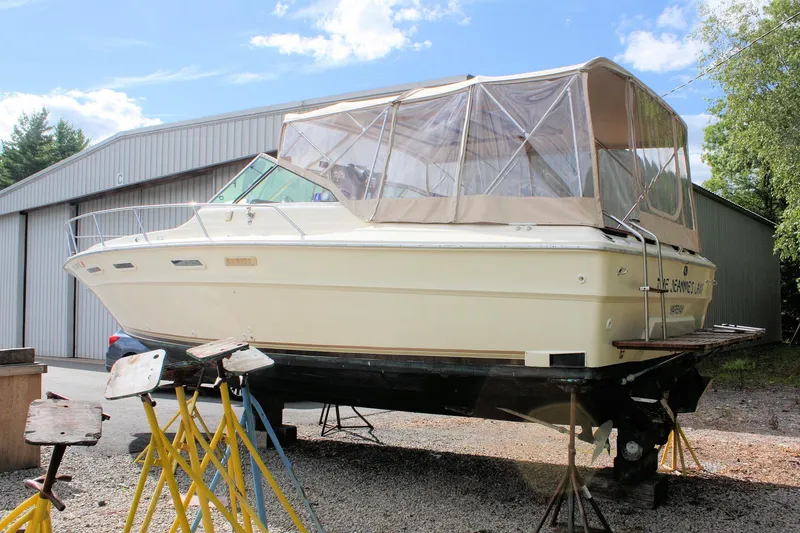 Slide: The Image of 1980 Sea Ray 300 Weekender boat on stands, with covered cockpit, near a metal building. - 2