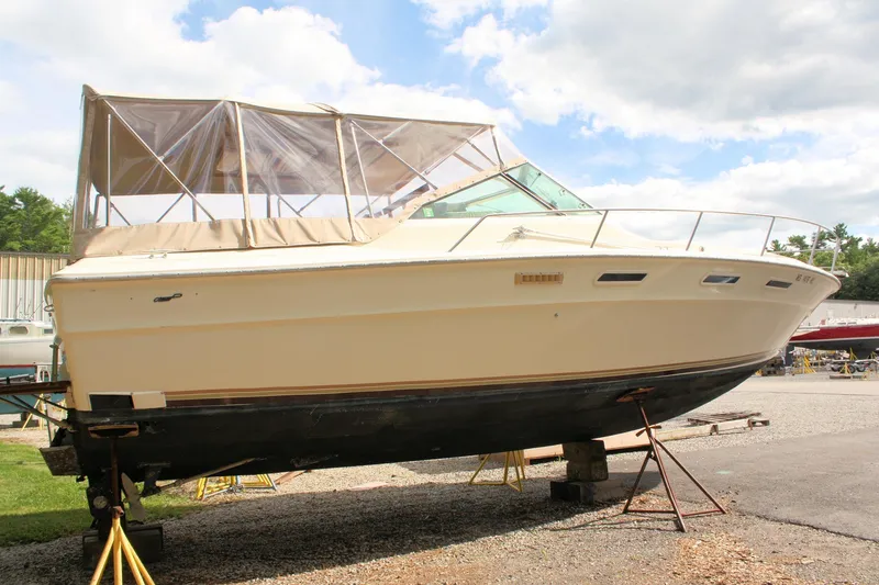 Slide: The Image of 1980 Sea Ray 300 Weekender boat on stands, beige hull, clear canopy, outdoor setting. - 3