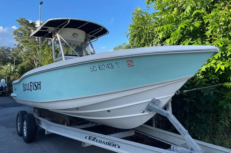 Slide: The Image of 2006 Scout 242 Sportfish boat on trailer, light blue hull, parked near greenery. - 6