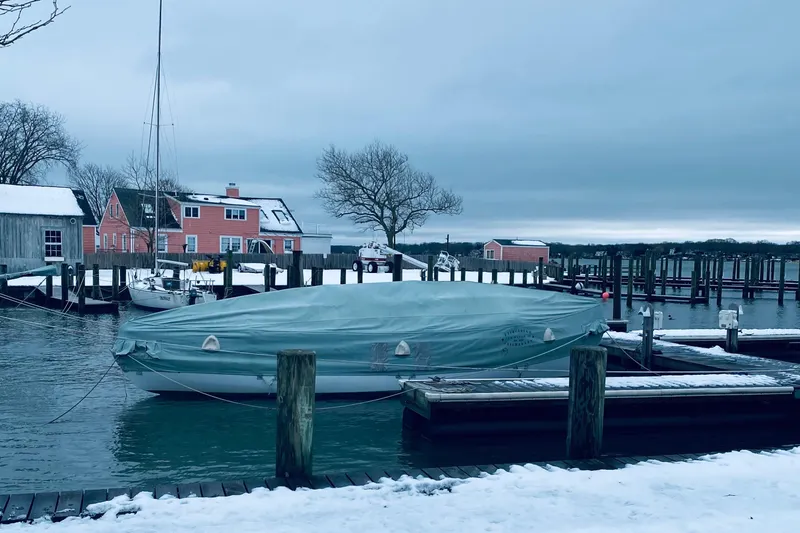 Slide: The Image of 1974 Herreshoff Rozinante sailboat covered at snowy dock, with colorful houses in the background. - 61