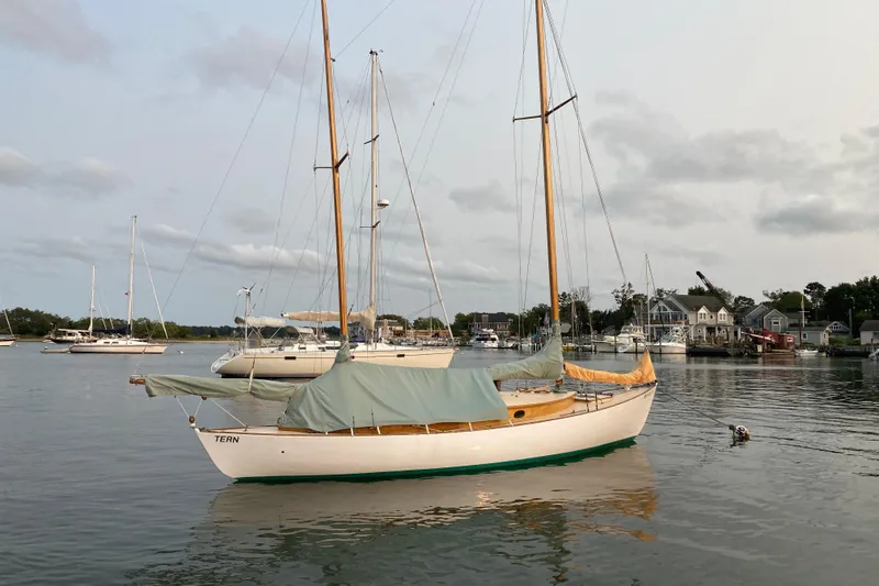 Slide: The Image of 1974 Herreshoff Rozinante sailboat moored in a calm harbor, surrounded by other boats. - 42