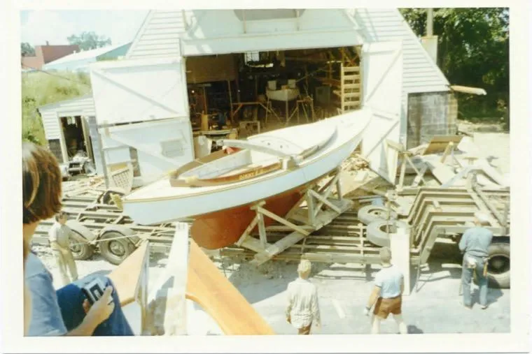 Slide: The Image of 1974 Herreshoff Rozinante sailboat being moved from a workshop, surrounded by people. - 74
