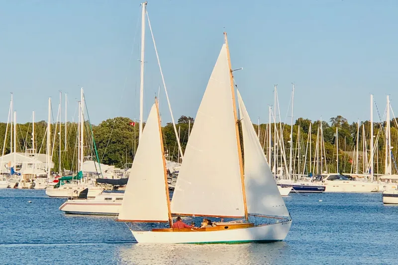 Slide: The Image of 1974 Herreshoff Rozinante sailboat on calm waters, surrounded by marina and sailboats. - 7