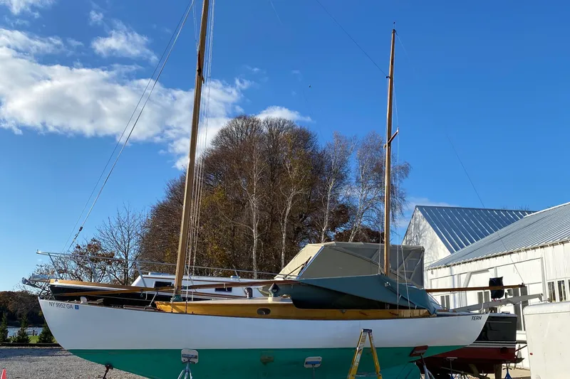 Slide: The Image of 1974 Herreshoff Rozinante sailboat on land, clear sky, trees, and building in background. - 55