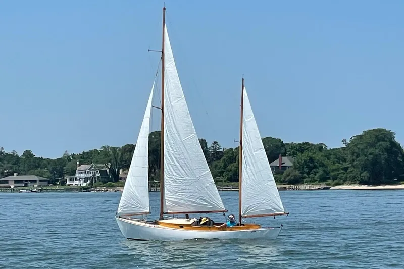 Slide: The Image of 1974 Herreshoff Rozinante sailboat on calm water, with scenic shoreline background. - 9