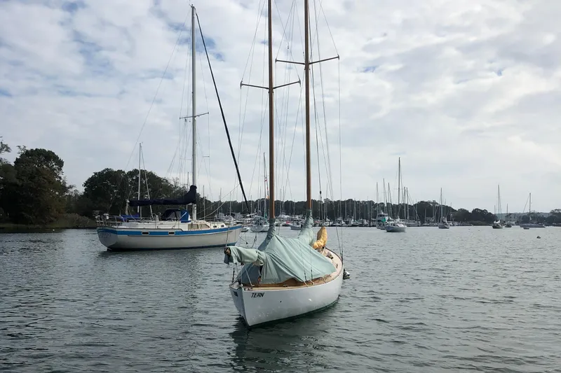 Slide: The Image of 1974 Herreshoff Rozinante sailboat moored in a scenic harbor with other boats. - 52