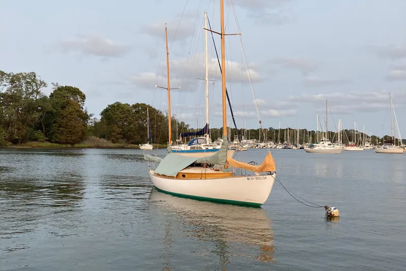 Slide: The Image of 1974 Herreshoff Rozinante sailboat moored on calm water with trees and other boats in background. - 47
