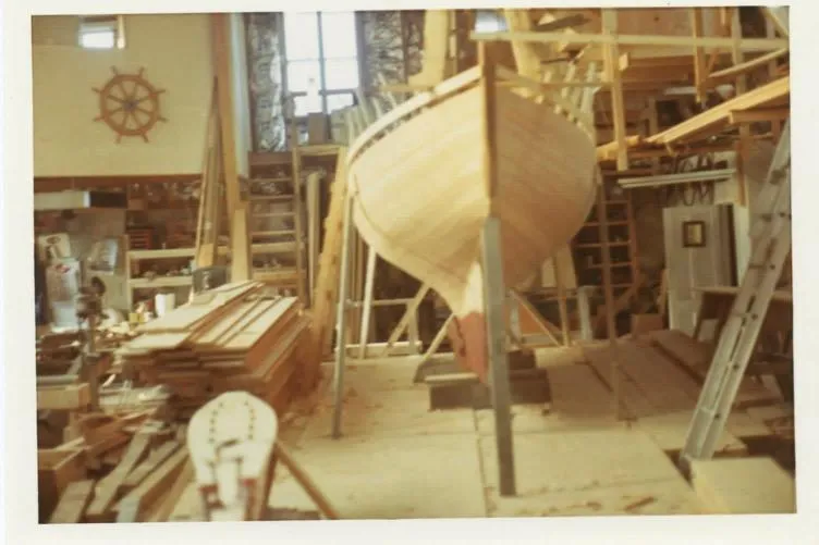 Slide: The Image of 1974 Herreshoff Rozinante sailboat under construction in a workshop with nautical decor. - 64