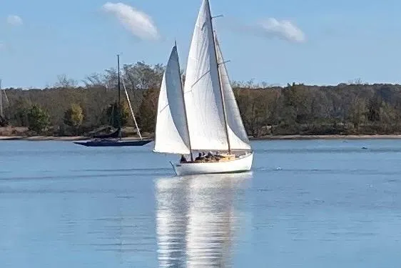 Slide: The Image of 1974 Herreshoff Rozinante sailboat gliding on calm water with trees in the background. - 8