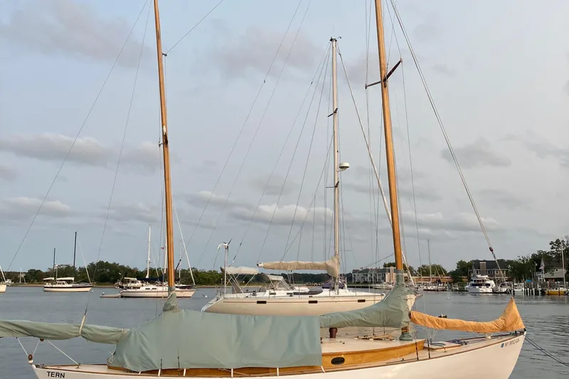 Slide: The Image of 1974 Herreshoff Rozinante sailboat docked in a serene marina setting. - 58