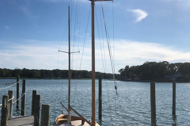 Slide: The Image of 1974 Herreshoff Rozinante sailboat docked by a serene lake under a clear blue sky. - 14