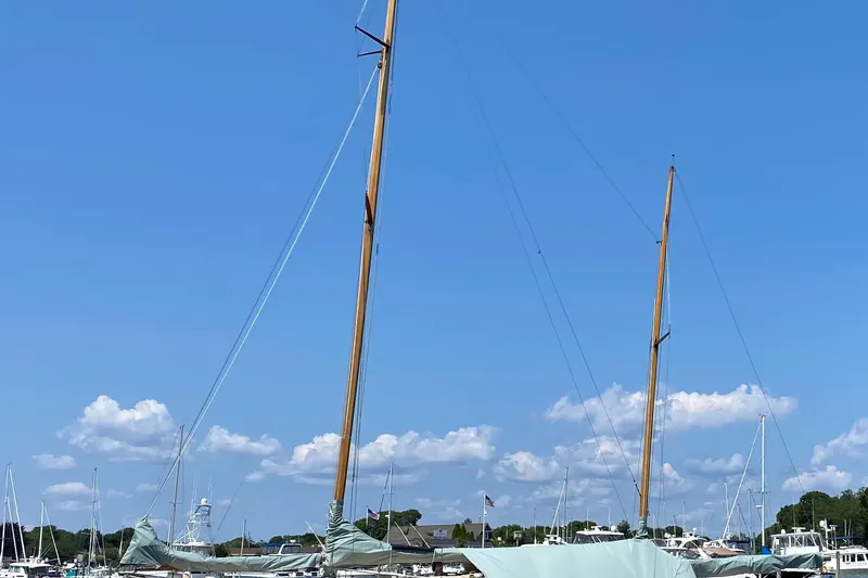 Slide: The Image of 1974 Herreshoff Rozinante sailboat with tall masts docked under clear blue sky. - 49