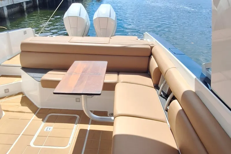 Slide: The Image of 2021 Aviara AV32 OB boat interior with tan seating and wooden table, docked by the water. - 16
