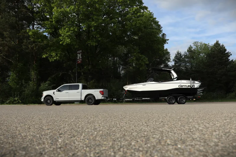 Slide: The Image of White truck towing 2025 Centurion Nv213 boat on a road with trees in the background. - 20