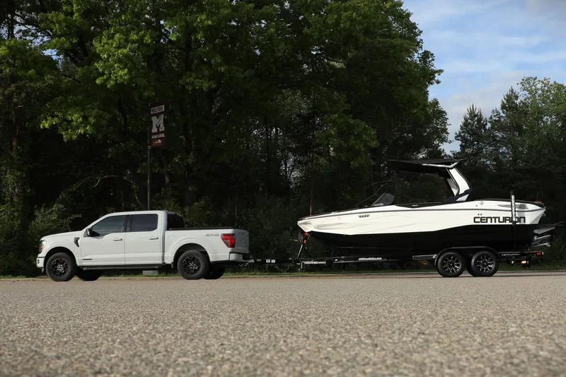 Slide: The Image of White truck towing 2025 Centurion Nv213 boat on a trailer, surrounded by trees. - 21