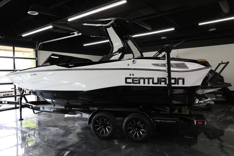 Slide: The Image of 2025 Centurion Nv213 boat in showroom, sleek black and white design on trailer. - 26