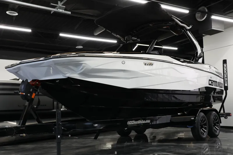 Slide: The Image of 2025 Centurion Nv213 boat on trailer in showroom, sleek black and white design. - 7