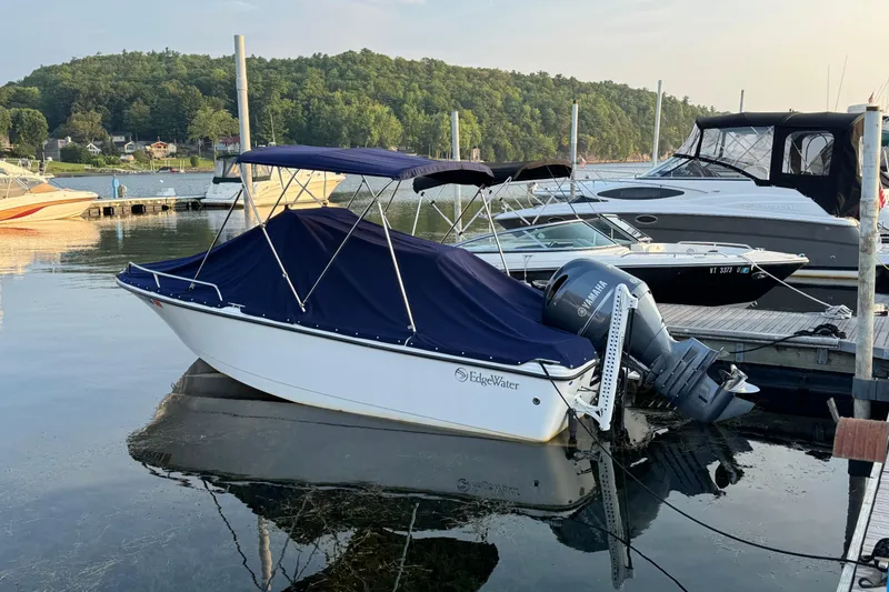 Slide: The Image of 2019 Edgewater 188CC boat docked with cover, surrounded by calm water and scenic greenery. - 16