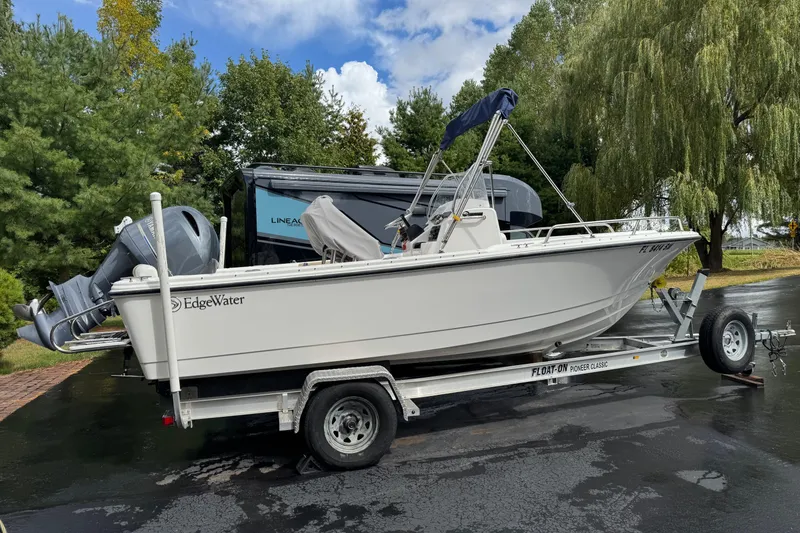 Slide: The Image of 2019 Edgewater 188CC boat on trailer, parked outdoors with trees in the background. - 2