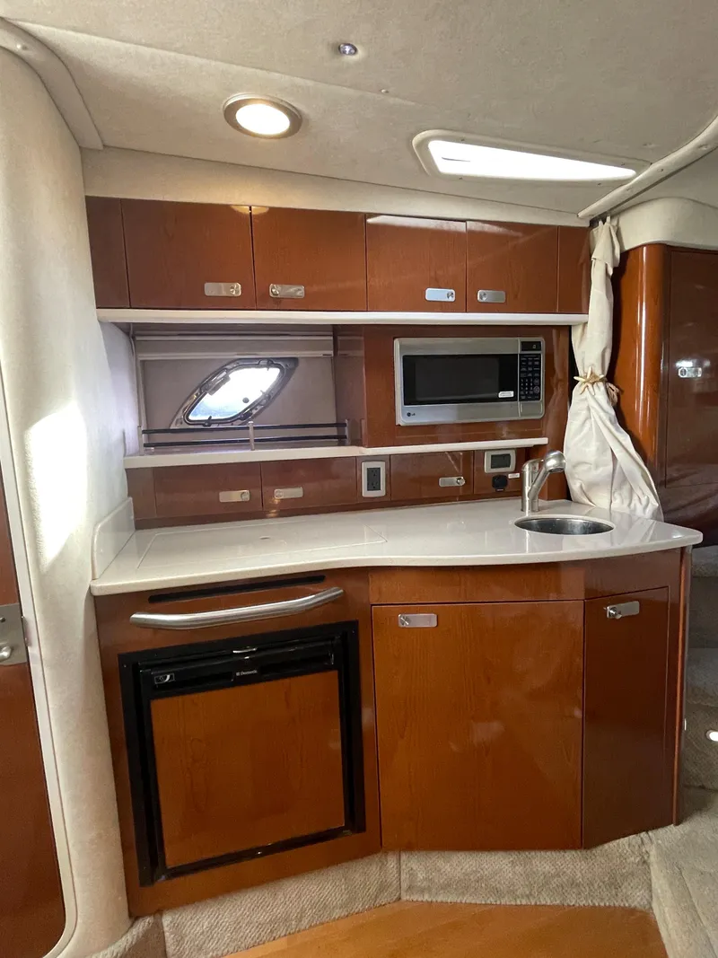 Slide: The Image of 2012 Sea Ray 330 Sundancer galley with wood cabinetry, microwave, sink, and mini-fridge. - 17