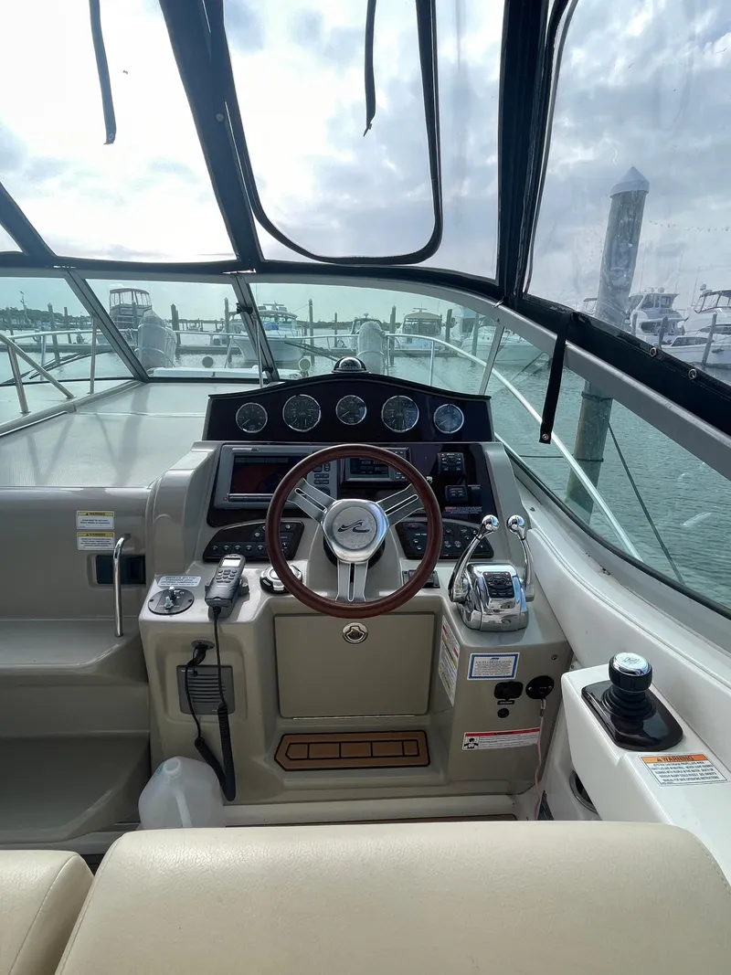 Slide: The Image of 2012 Sea Ray 330 Sundancer helm with steering wheel and control panel, docked at marina. - 4