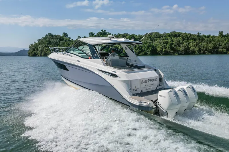 Slide: The Image of 2022 Sea Ray Sundancer 320 Outboard cruising on a scenic lake with lush greenery. - 9