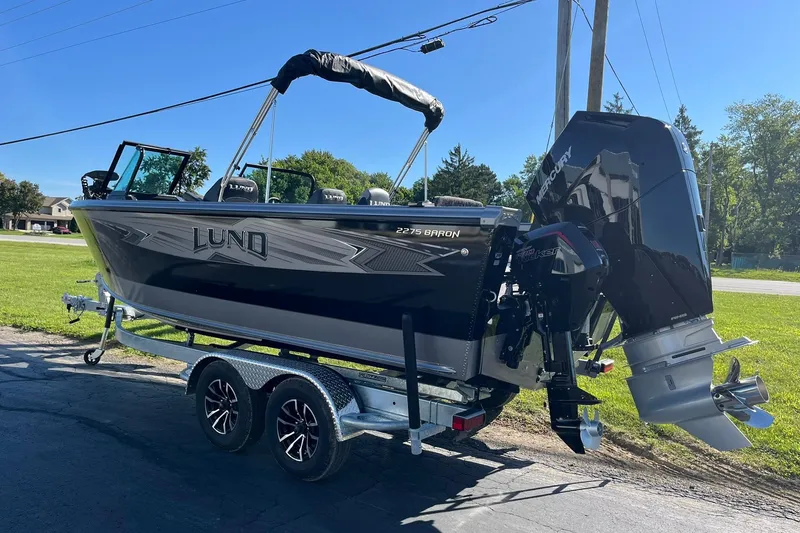 Slide: The Image of 2026 Lund 2275 Baron boat on trailer, parked outdoors, featuring a powerful Mercury engine. - 3
