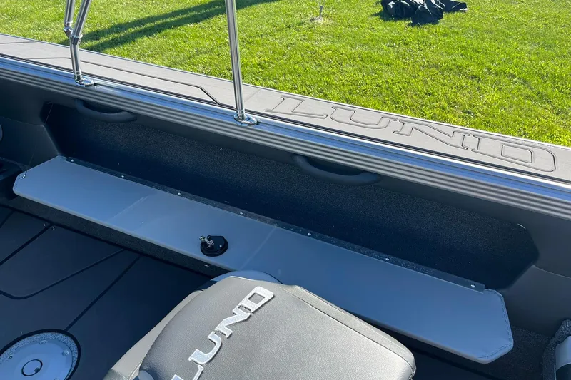Slide: The Image of 2026 Lund 2275 Baron boat interior with branded seating and storage, on grassy background. - 34