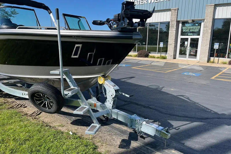 Slide: The Image of 2026 Lund 2275 Baron boat on trailer outside dealership, sunny day. - 4