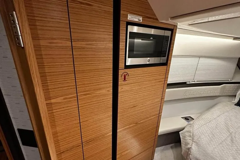 Slide: The Image of 2023 Tiara Yachts 43 LS interior with wood paneling, microwave, and cozy sleeping area. - 24