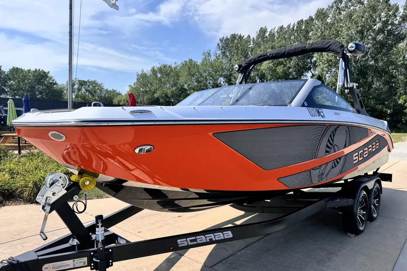 Slide: The Image of 2026 Scarab 235 LX Wake boat in vibrant orange on a trailer, outdoors. - 2