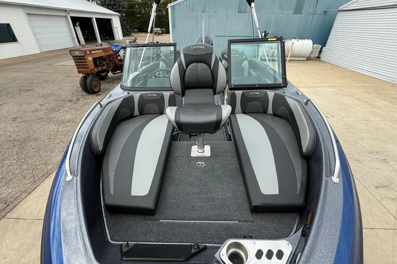 Slide: The Image of 2026 Lund 189 Tyee GL boat interior with gray seating and windshield, parked near a garage. - 9