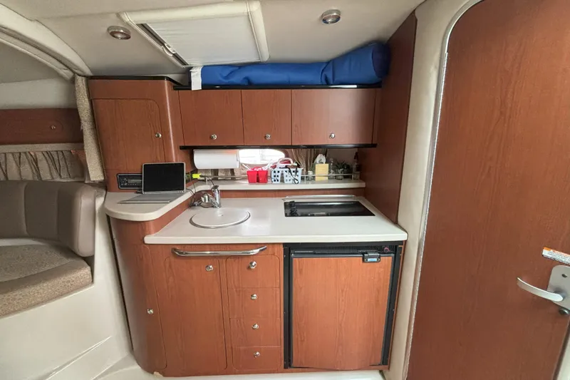 Slide: The Image of 2003 Chaparral 310 Signature boat interior with kitchenette, featuring wood cabinets and compact appliances. - 4