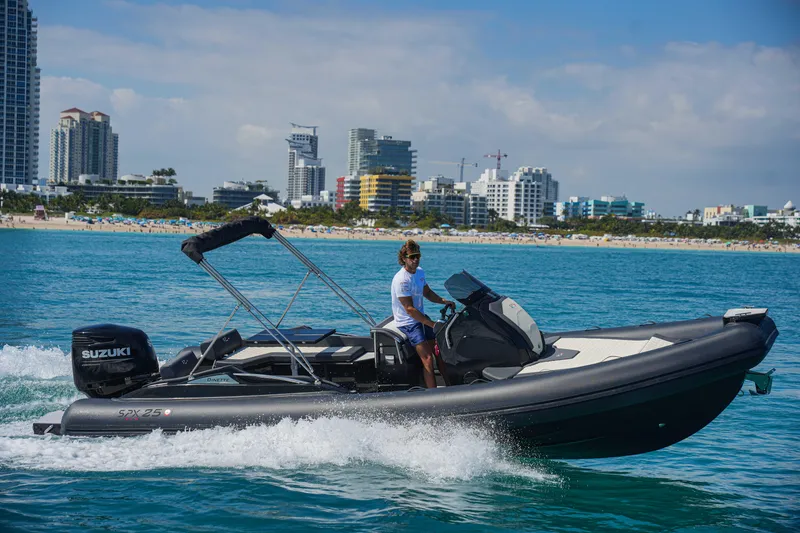 The Image of 2023 SPX RIB 25 Dinette boat cruising near a city shoreline. - 0