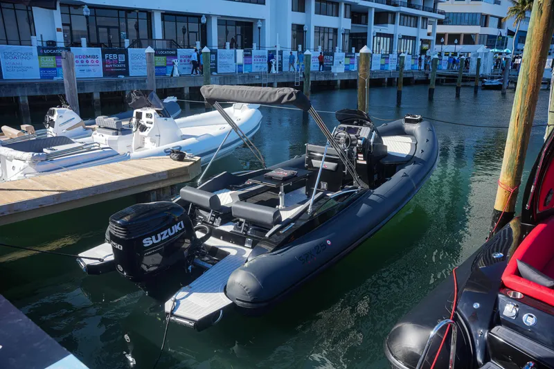 Slide: The Image of 2023 SPX RIB 25 Dinette boat docked, featuring a Suzuki outboard motor. - 5
