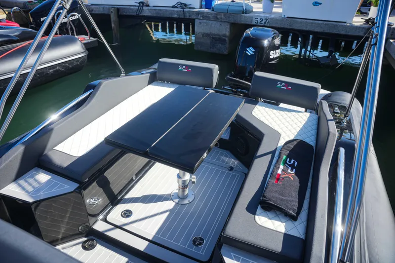 Slide: The Image of 2023 SPX RIB 25 Dinette boat interior with seating and table, docked at marina. - 9