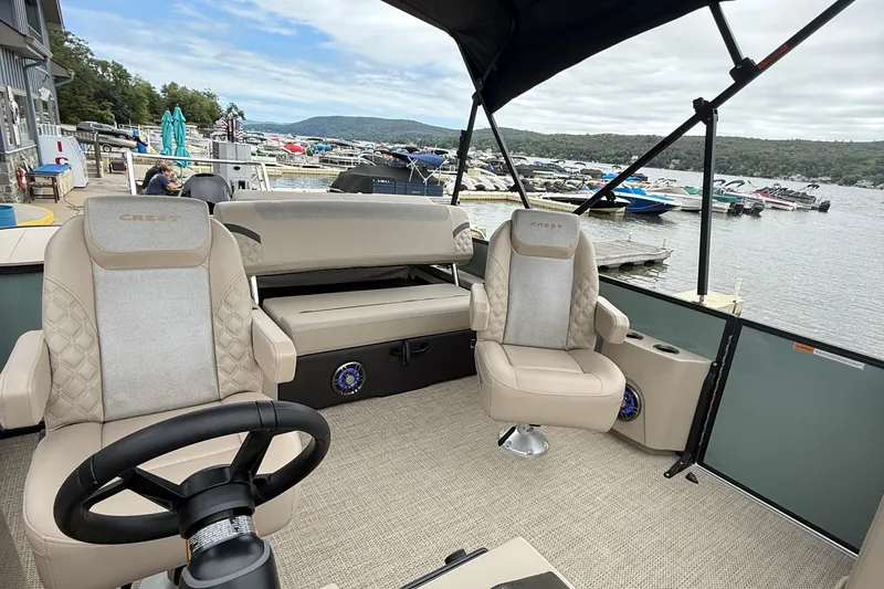 Slide: The Image of 2026 Crest 230 SLSC boat interior with plush seating, docked at a scenic marina. - 6