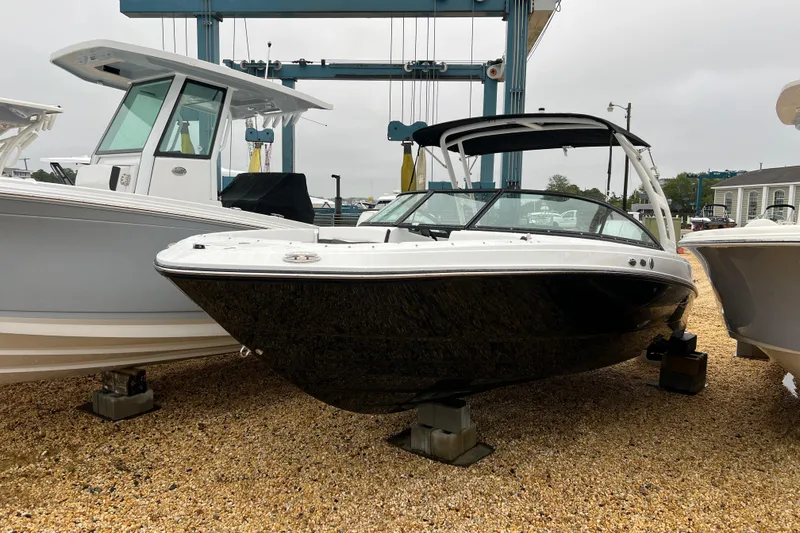 Slide: The Image of 2026 Monterey M-225 boat displayed on gravel, surrounded by other boats. - 2