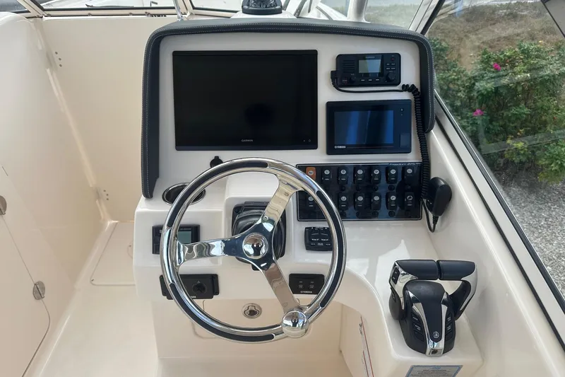 Slide: The Image of 2022 Grady-White Freedom 275 boat dashboard with steering wheel and electronic controls. - 4