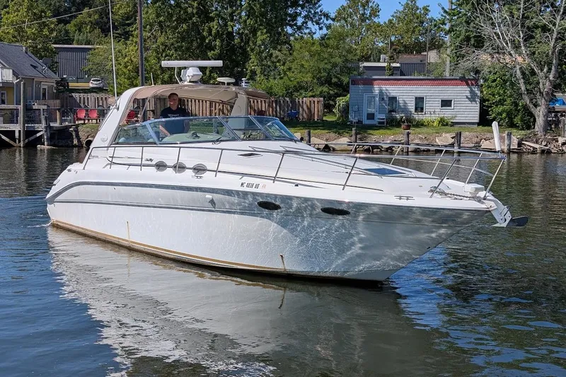 Slide: The Image of 1998 Sea Ray 370 Sundancer yacht cruising on a calm river near a residential area. - 1