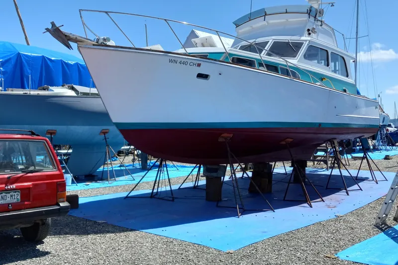 Slide: The Image of 1968 Egg Harbor Sedan boat on stands, with a red vehicle nearby, in a boatyard. - 25