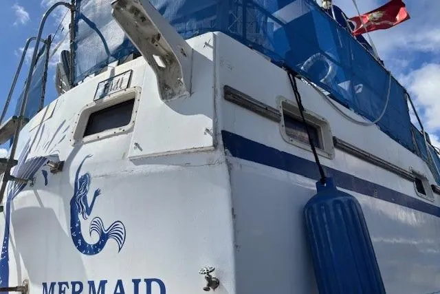 Slide: The Image of 1979 Custom Sun Harbor Sundeck Trawler with "Mermaid" logo and blue accents, docked under clear skies. - 34