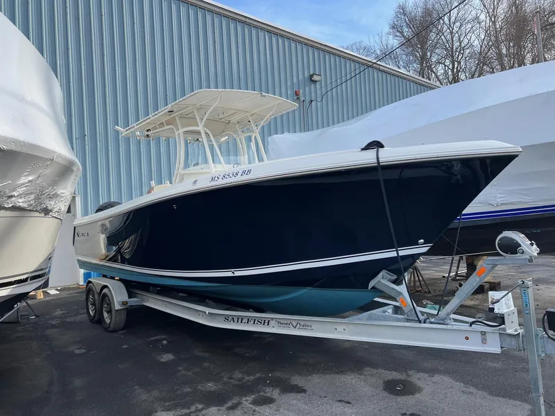 Slide: The Image of 2013 Sailfish 270 CC boat on trailer, parked outdoors near a metal building. - 2