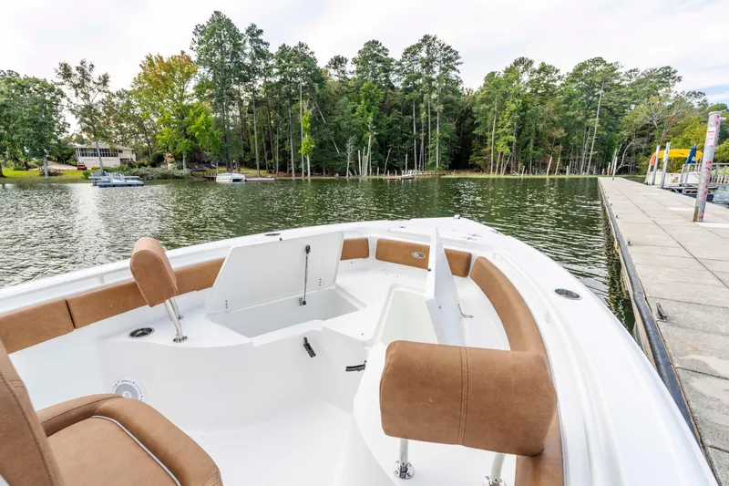 Slide: The Image of 2026 Sea Hunt Ultra 235 SE boat docked by a scenic lakeside with lush trees. - 2