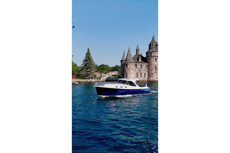 Slide: The Image of 2024 DaVinci 30HT boat cruising near a historic castle on a sunny day. - 2
