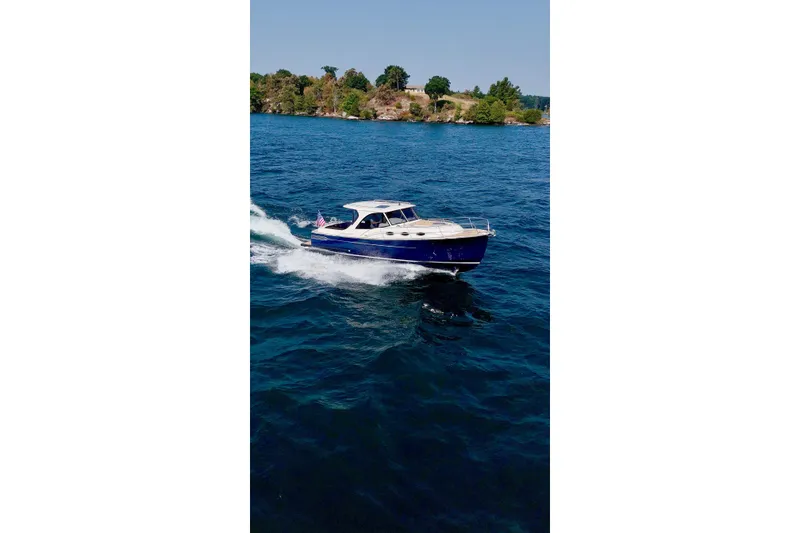 Slide: The Image of 2024 DaVinci 30HT boat cruising on a clear blue lake with scenic shoreline. - 7