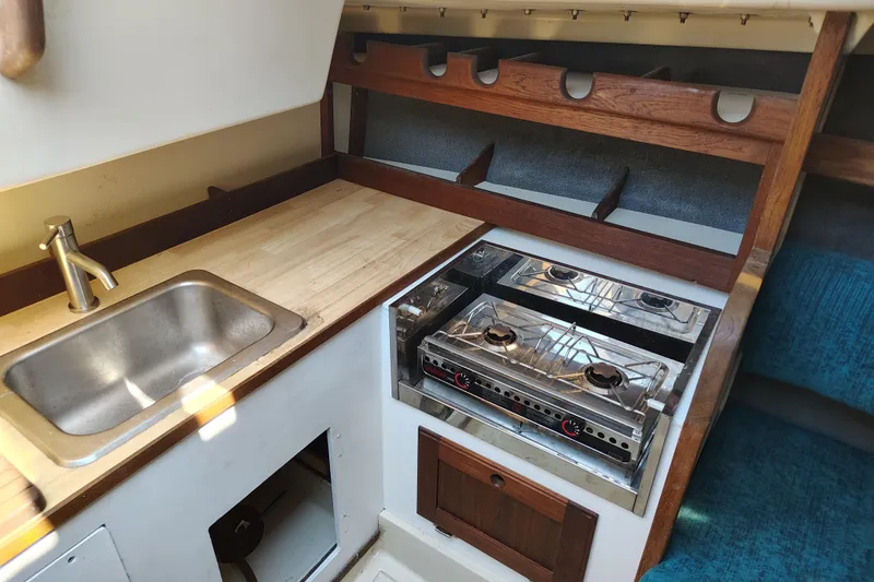 Slide: The Image of 1979 O'Day 28 sailboat galley with sink, stove, and wooden storage shelves. - 20