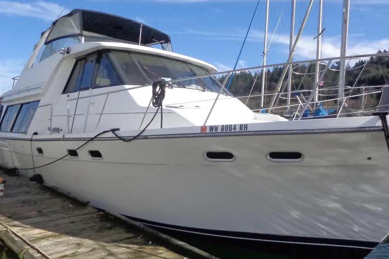 The Image of 1999 Bayliner 4788 Pilot House Motoryacht docked in a marina under clear skies. - 0