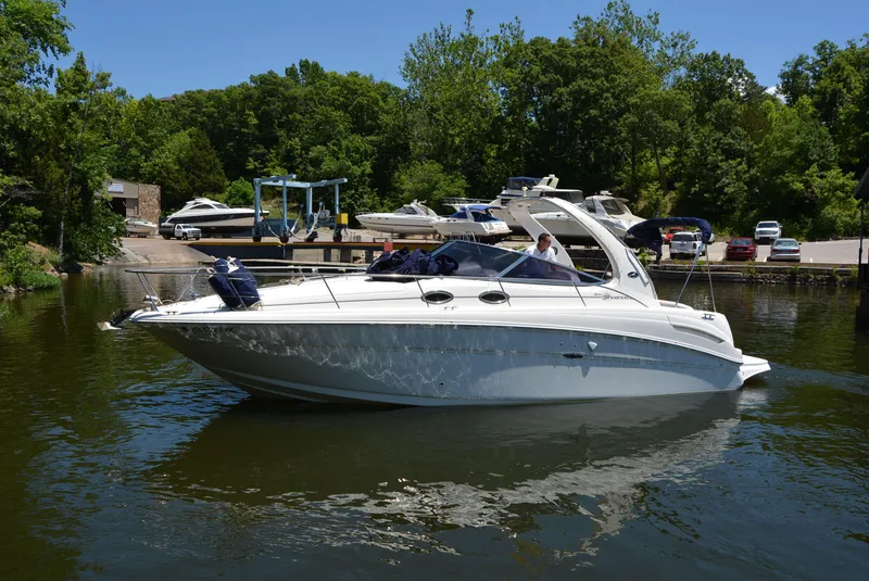 Slide: The Image of 2004 Sea Ray 300 Sundancer boat docked on a calm lake with lush greenery. - 1